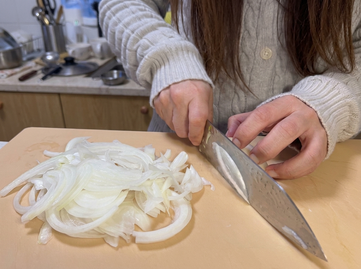 Fette di cipolla fresca tagliate sottili su un tagliere chiaro, pronte per la cottura.