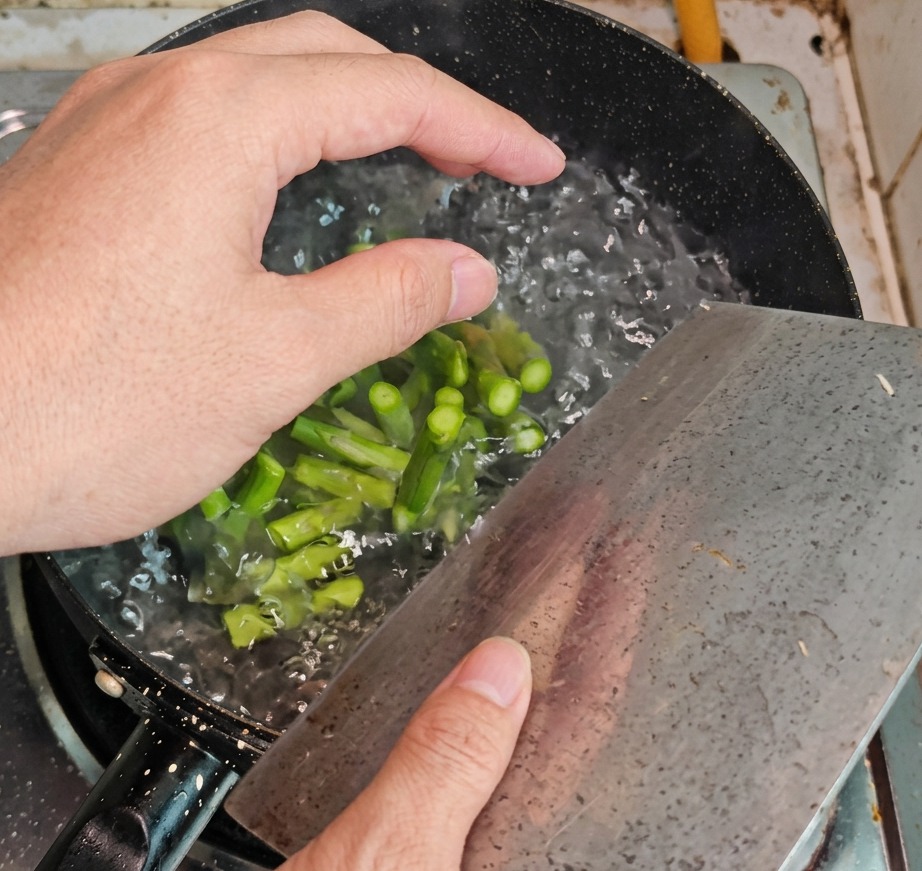 Sezioni di asparagi verdi rimosse da una pentola di acqua bollente con una schiumarola.