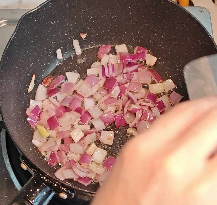 Pancetta e cipolla a dadini che soffriggono insieme in una padella a fuoco vivo.