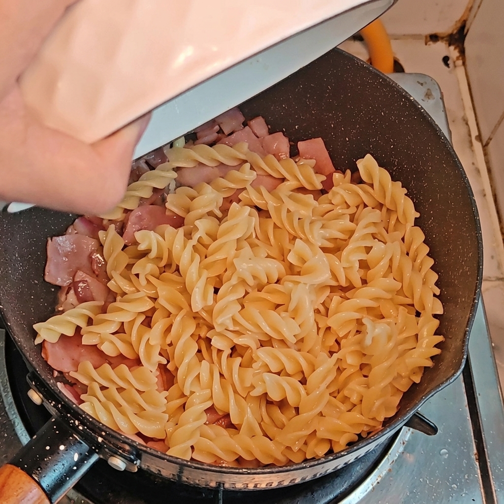Fusilli e asparagi aggiunti in padella insieme alla pancetta e alle cipolle.