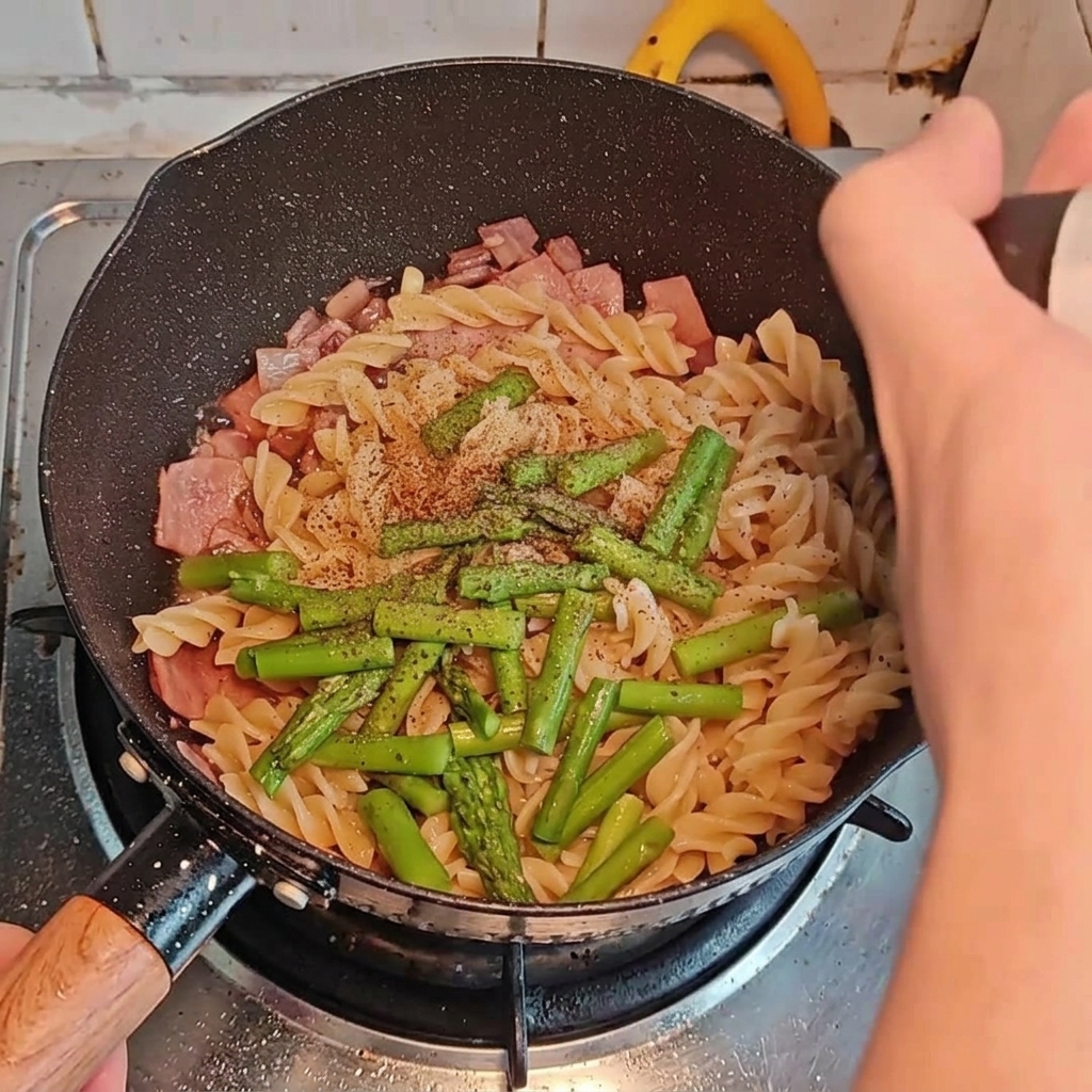 Condimenti aggiunti sopra la pasta, la pancetta e gli asparagi nella padella.