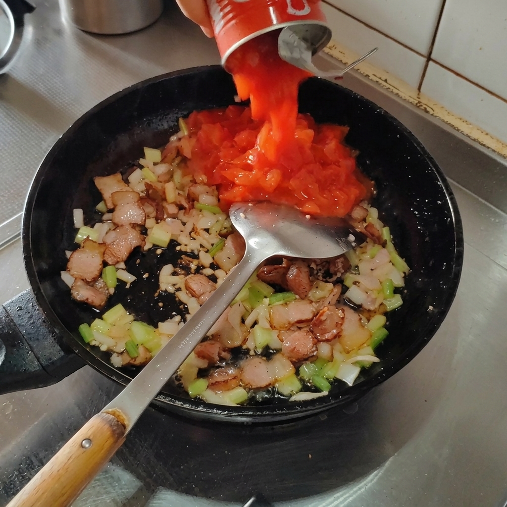 Pomodori pelati versati nella padella con la pancetta e gli odori.