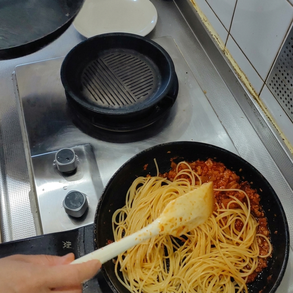 Spaghetti cotti versati nella padella con il sugo di pomodoro e pancetta.