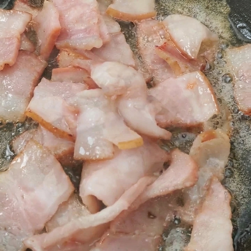 Pomodorini tagliati a metà che cuociono in padella insieme alla pancetta croccante.