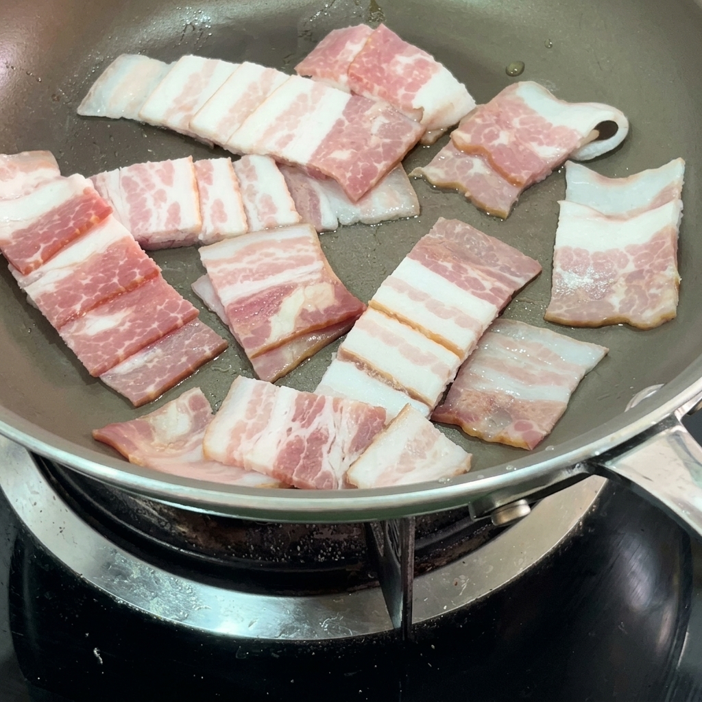 Strisce di pancetta che sfrigolano in padella.