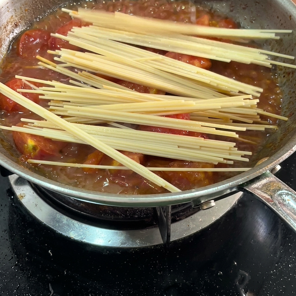 Spaghetti crudi immersi nel sugo di pomodoro in padella.