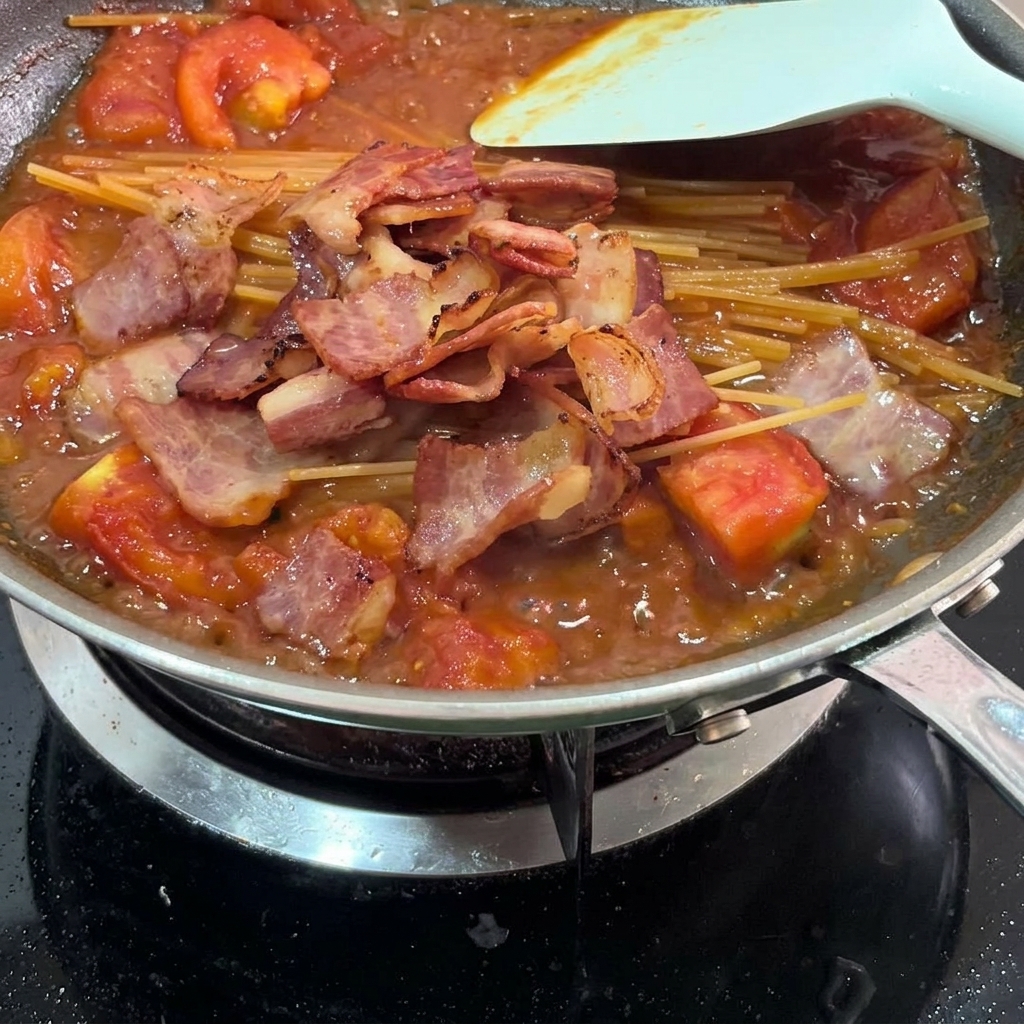Pezzi di pancetta croccante sparsi sulla pasta nel sugo.