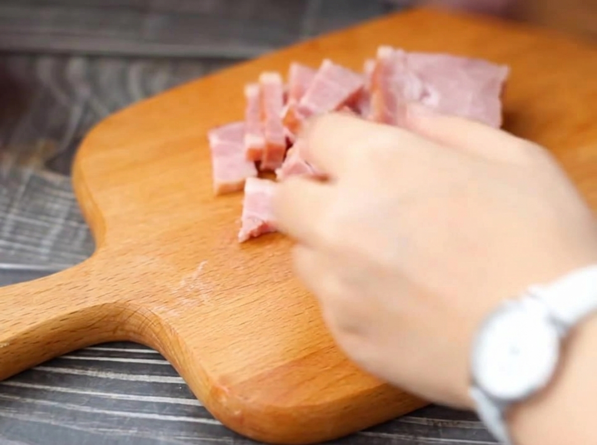 Strisce di pancetta tagliate in piccoli pezzi su un tagliere di legno.