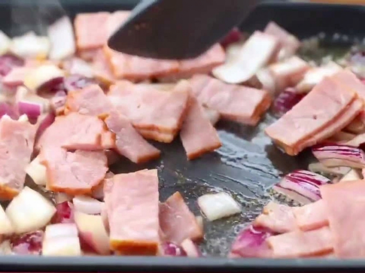 Pancetta e cipolla che cuociono insieme nella padella.