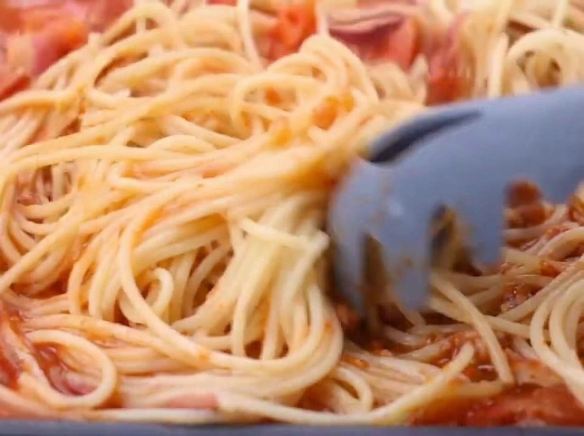 Spaghetti cotti che vengono trasferiti nella padella con il sugo di pomodoro e pancetta.
