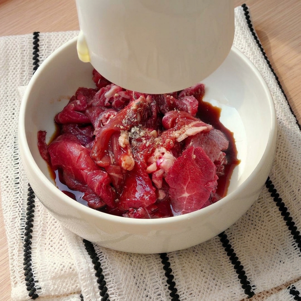 Fettine di manzo crudo in una ciotola bianca mentre vengono condite con ingredienti liquidi e spezie.