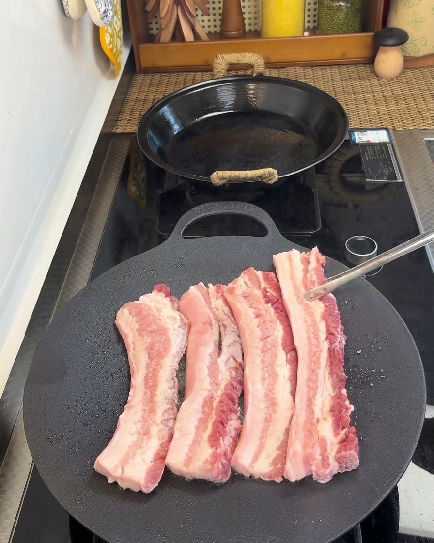 Pinze che girano le strisce di pancetta nella padella, rivelando il lato cotto e dorato.