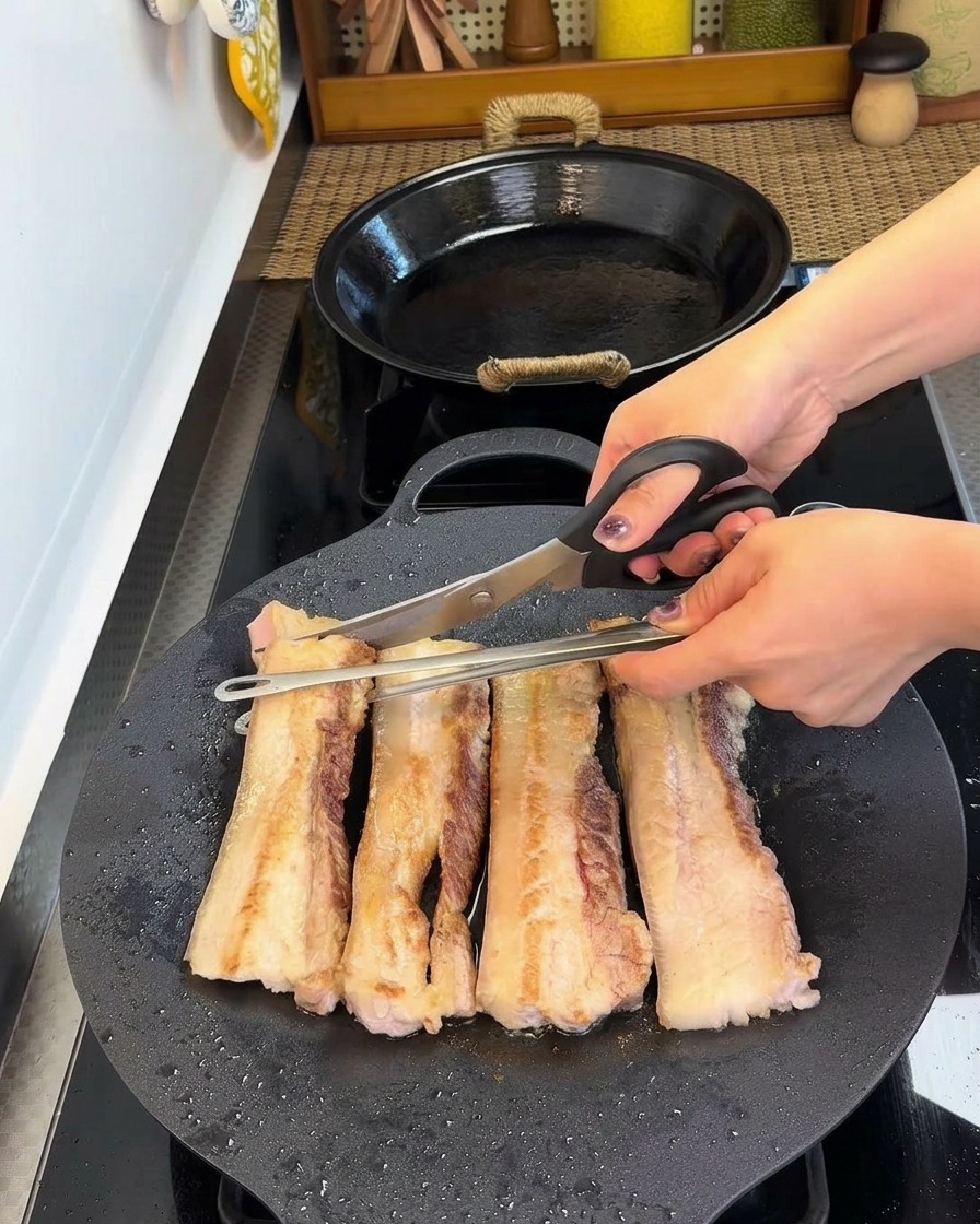 Forbici da cucina che tagliano le strisce di pancetta rosolate in piccoli pezzi direttamente nella padella.
