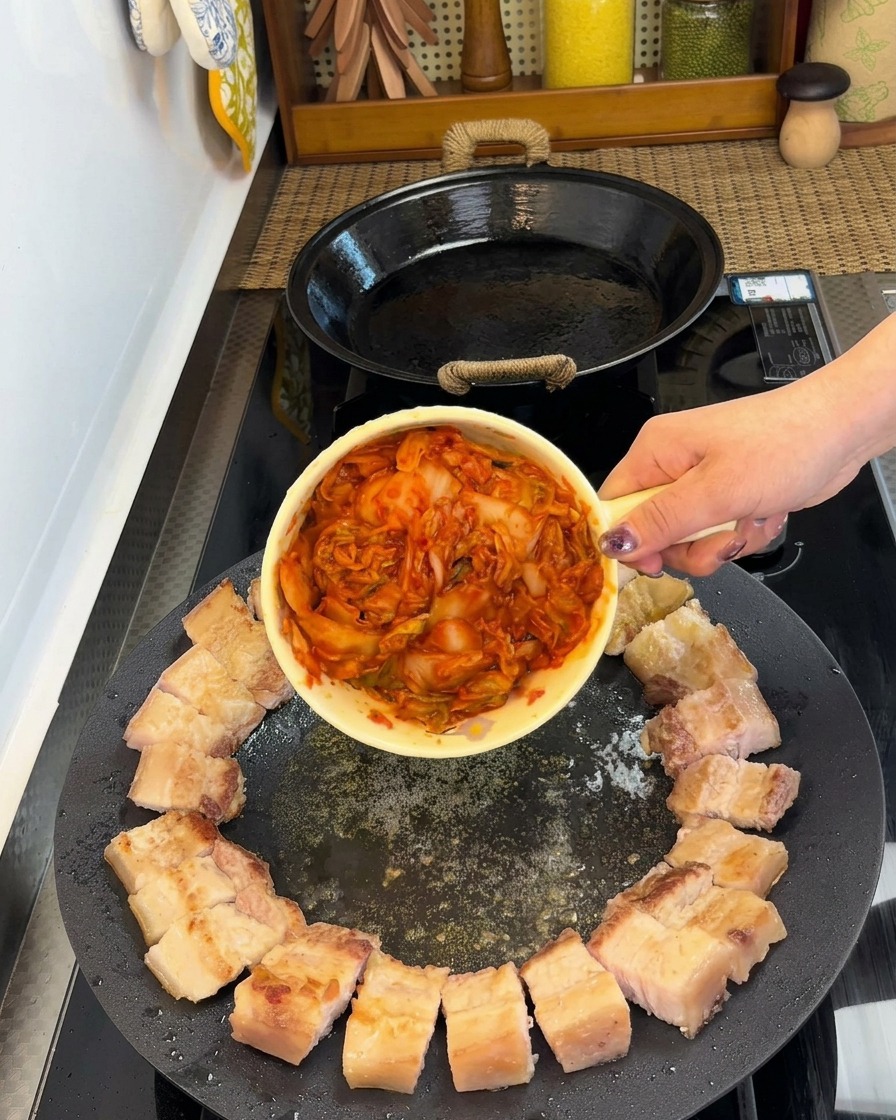 Pezzi di pancetta disposti a cerchio con una porzione di kimchi al centro della padella.