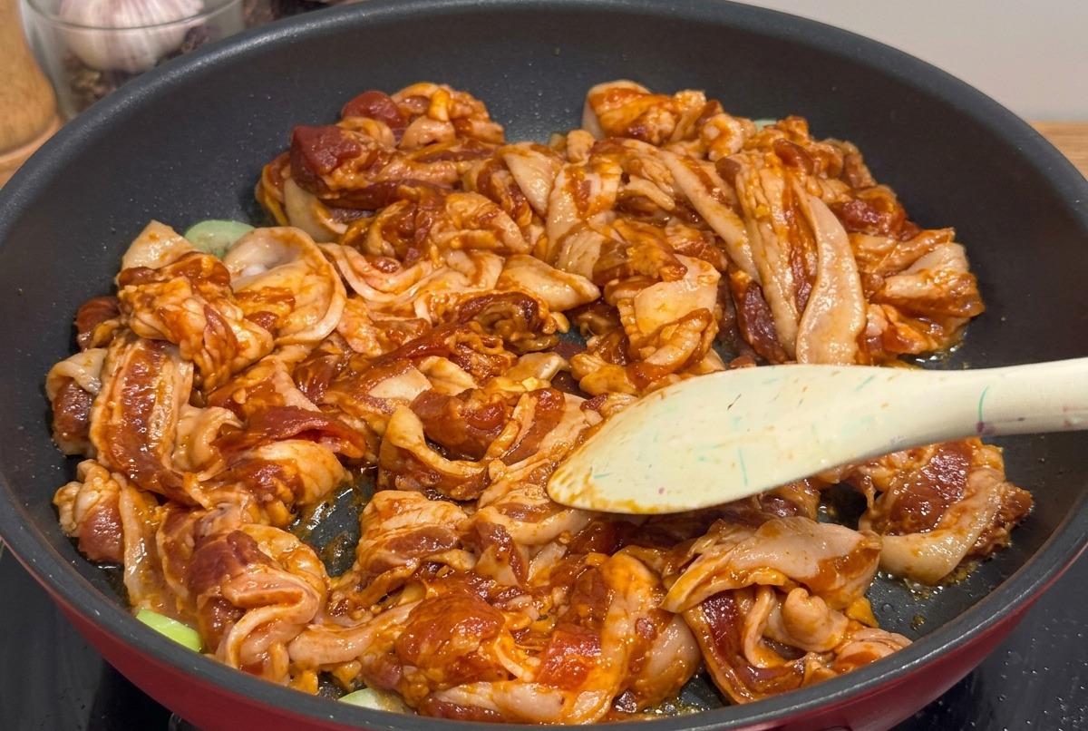 Pezzi di pancetta grigliata e glassata tagliati con forbici da cucina direttamente in padella.