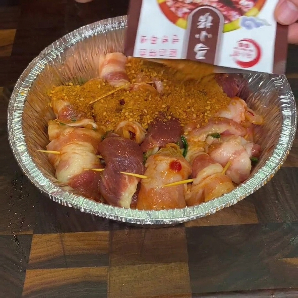 Mix di spezie per barbecue cosparso da una bustina sugli involtini di pancetta crudi in una vaschetta di alluminio.