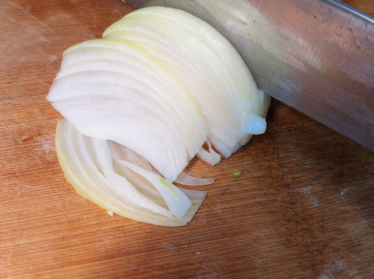 Strisce sottili di cipolla fresca appena affettate su un tagliere di legno.