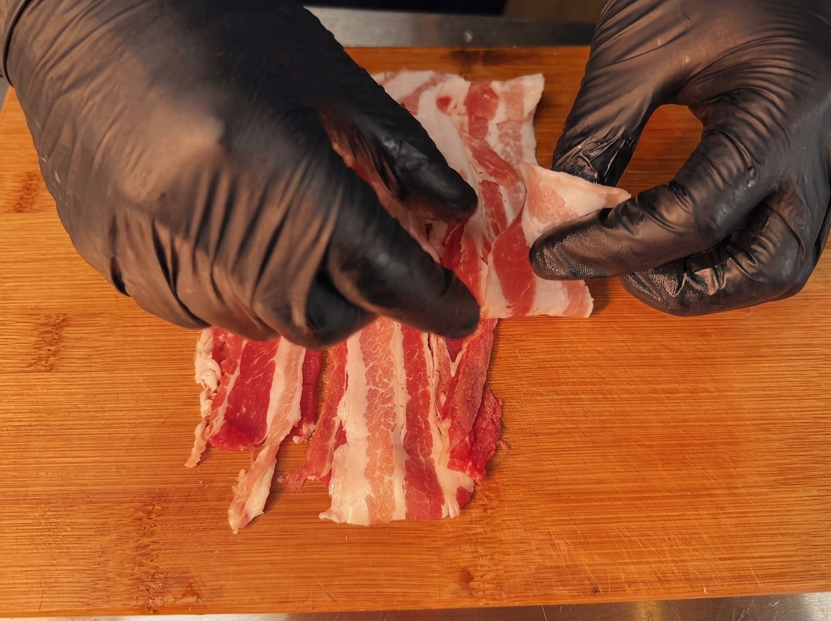 Fette sovrapposte di pancetta cruda pronte per il processo di arrotolamento.