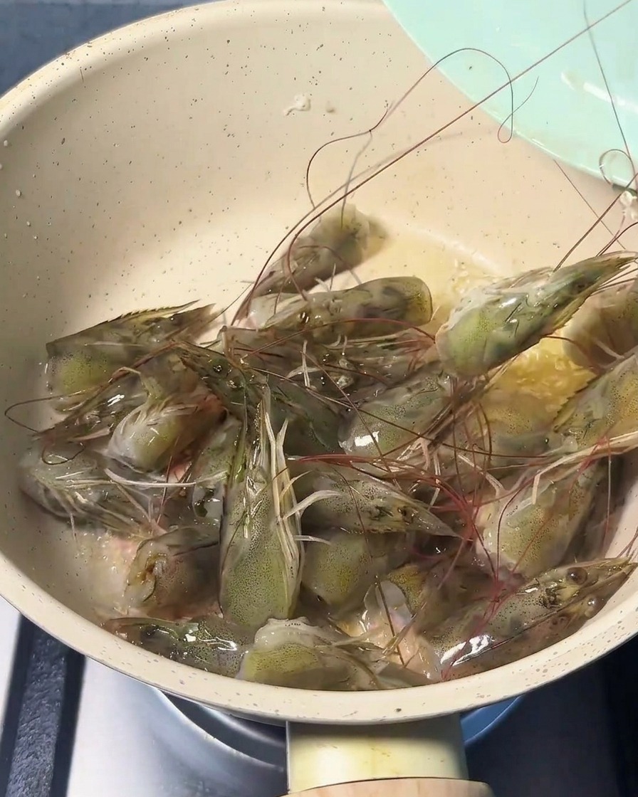 Teste di gambero fresche che sfrigolano in padella con olio, diventando rosa e sprigionando il loro aroma.