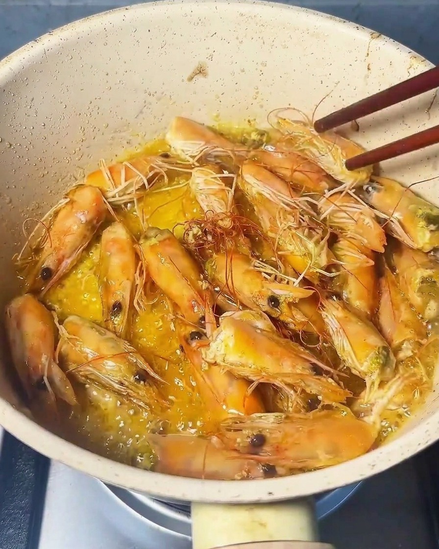 Primo piano di teste di gambero pressate con una spatola in padella, che rilasciano un olio dai toni arancioni.