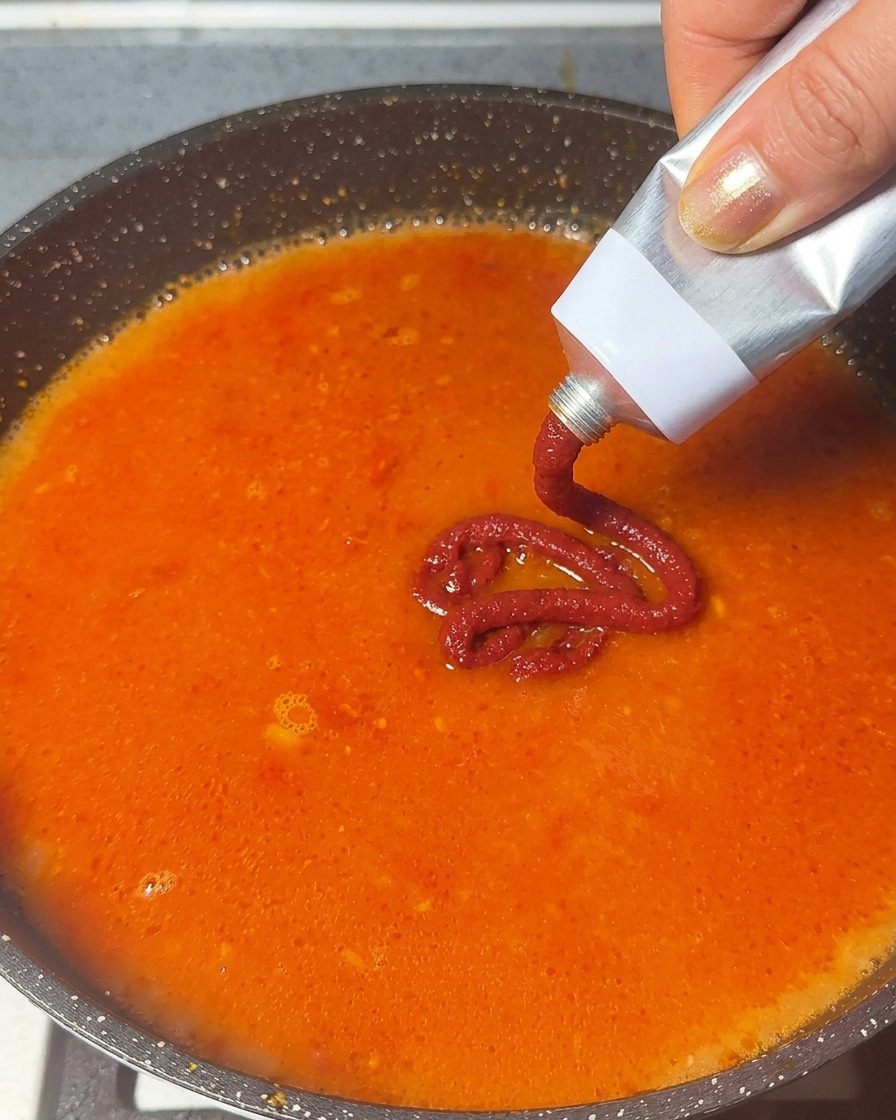 Concentrato di pomodoro spremuto da un tubetto di metallo in una base per zuppa rosso-arancio in ebollizione.