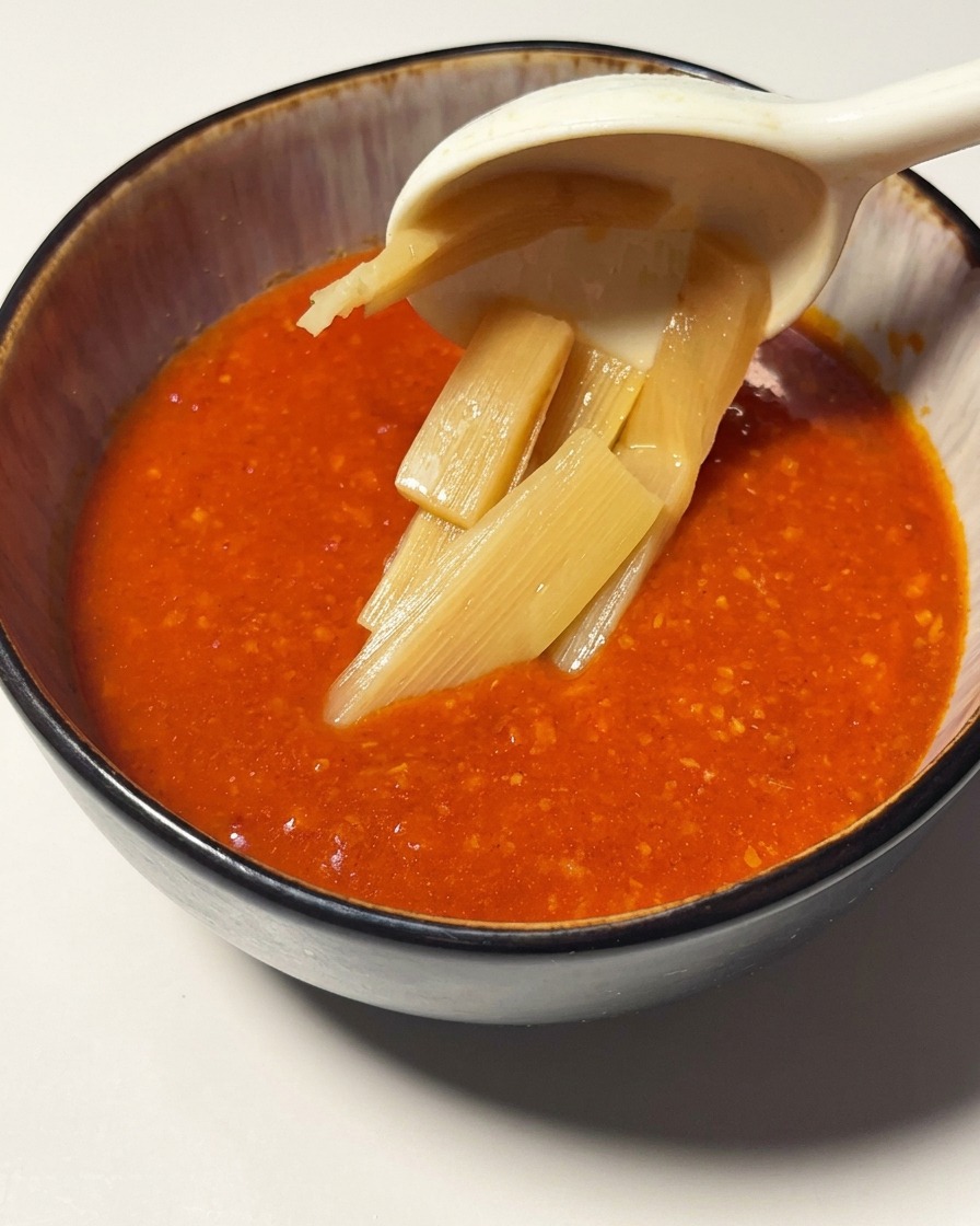 Fette di germogli di bambù sollevate da un cucchiaio in una ciotola piena di vivace salsa di pomodoro e gamberi.