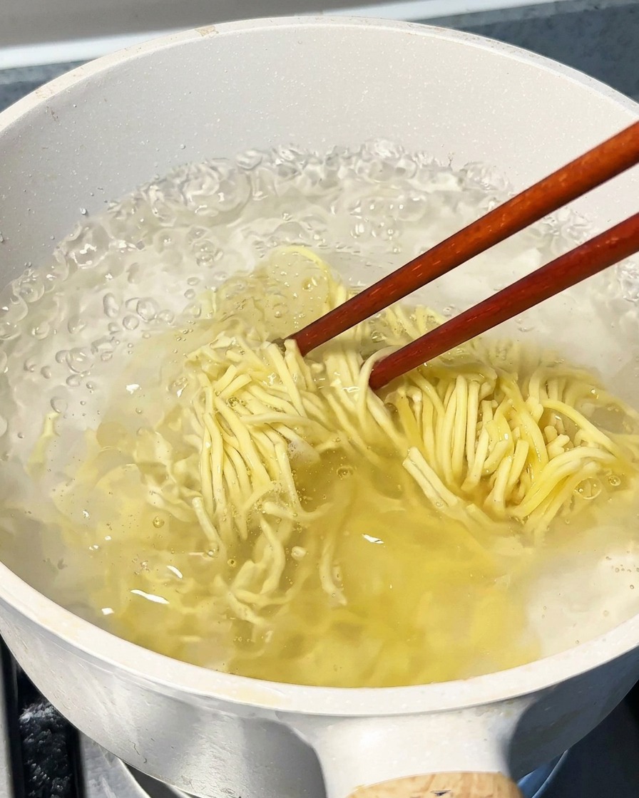 Noodles che bollono in una grande pentola dacqua, mescolati con bacchette di legno.
