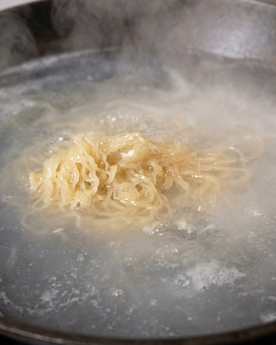 Noodles cotti sollevati dallacqua bollente per essere scolati.