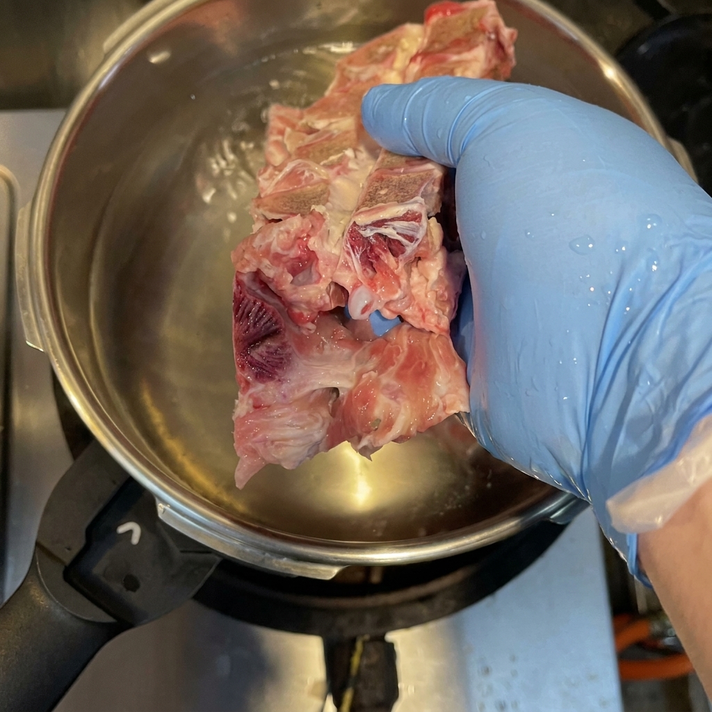 Ossa di maiale, carcassa di pollo e zampetti che bollono in una pentola a pressione per rimuovere le impurità.