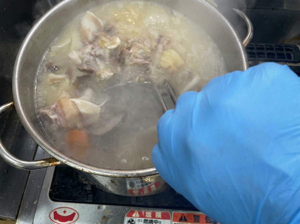 Mescolamento energico del brodo denso e cremoso in una grande pentola dacciaio.