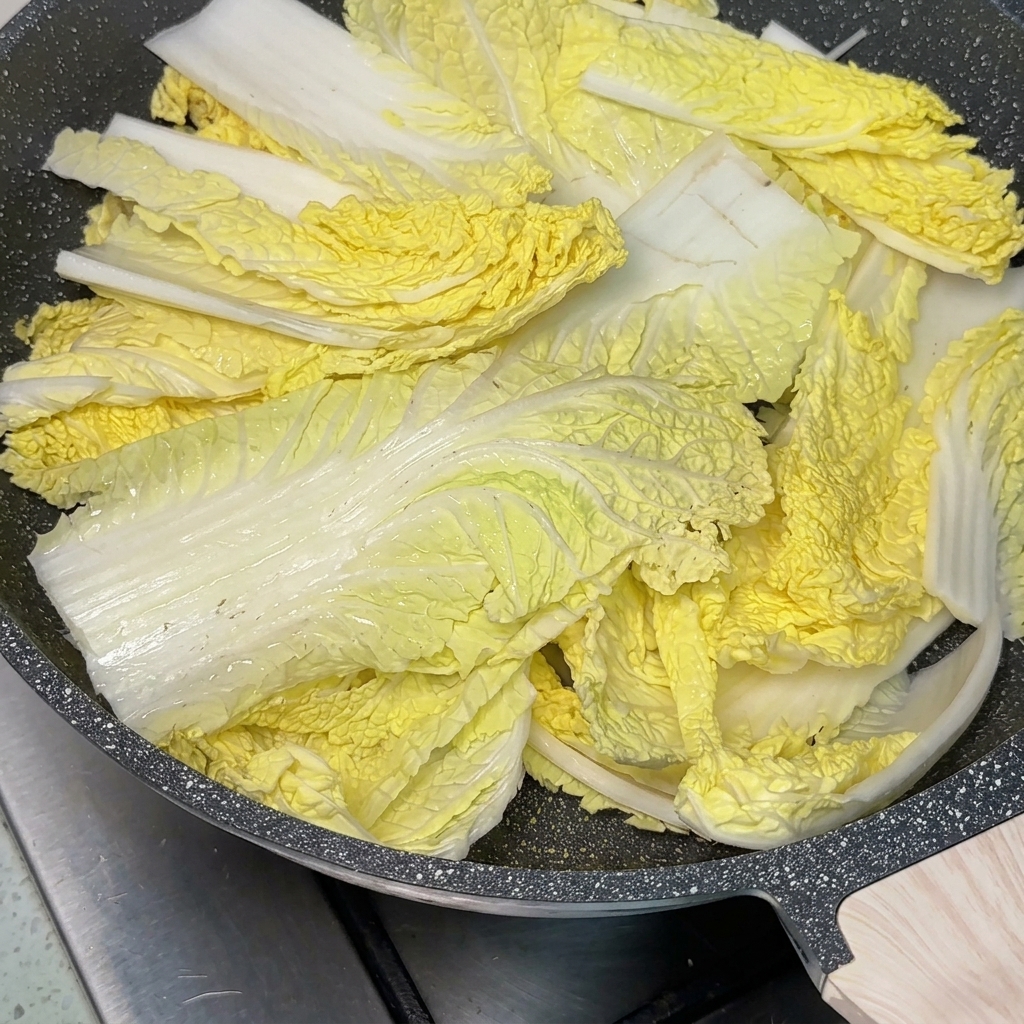 La padella con gli ingredienti dello stufato, un abbondante cucchiaio di pasta di peperoncino al centro, mentre viene versato il brodo.