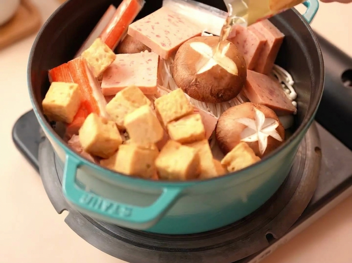 Cubetti di tofu di pesce e bastoncini di granchio sistemati in una pentola con Spam e funghi.