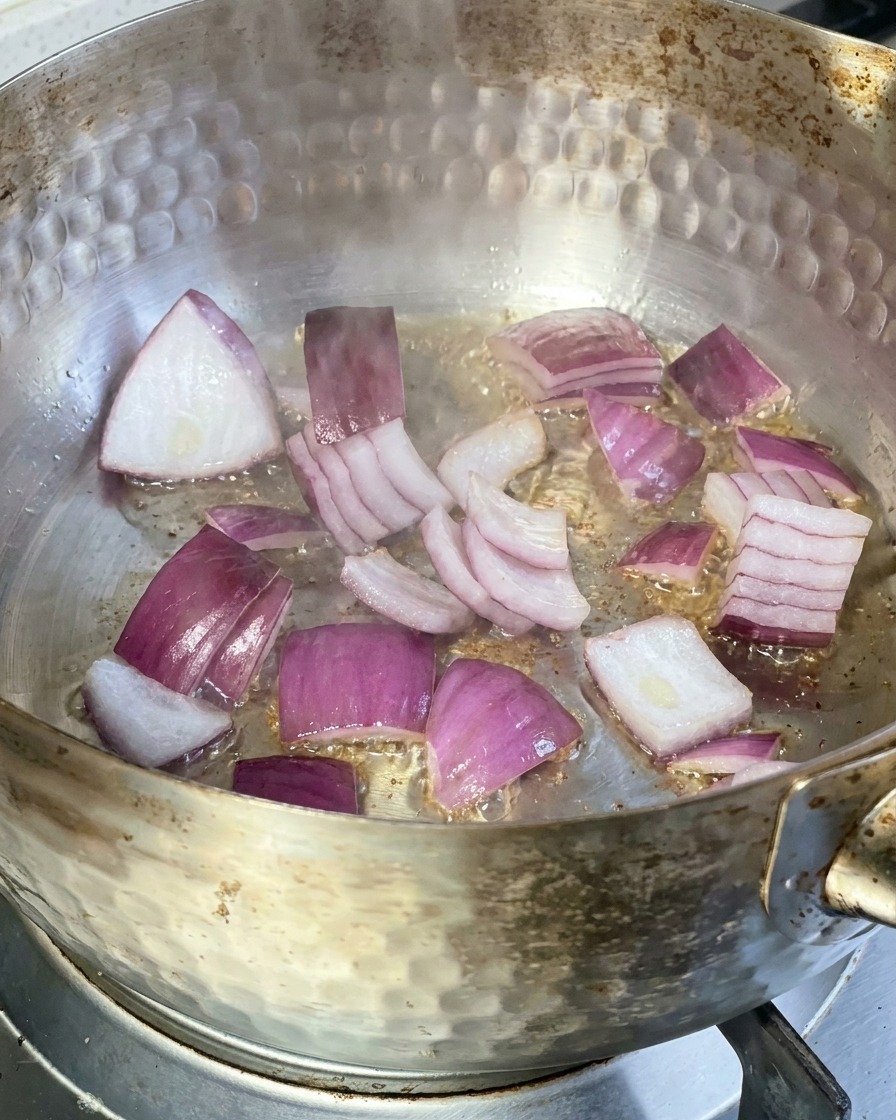 Fette di cipolla rossa che sfrigolano in una padella di metallo con olio caldo sul fornello.