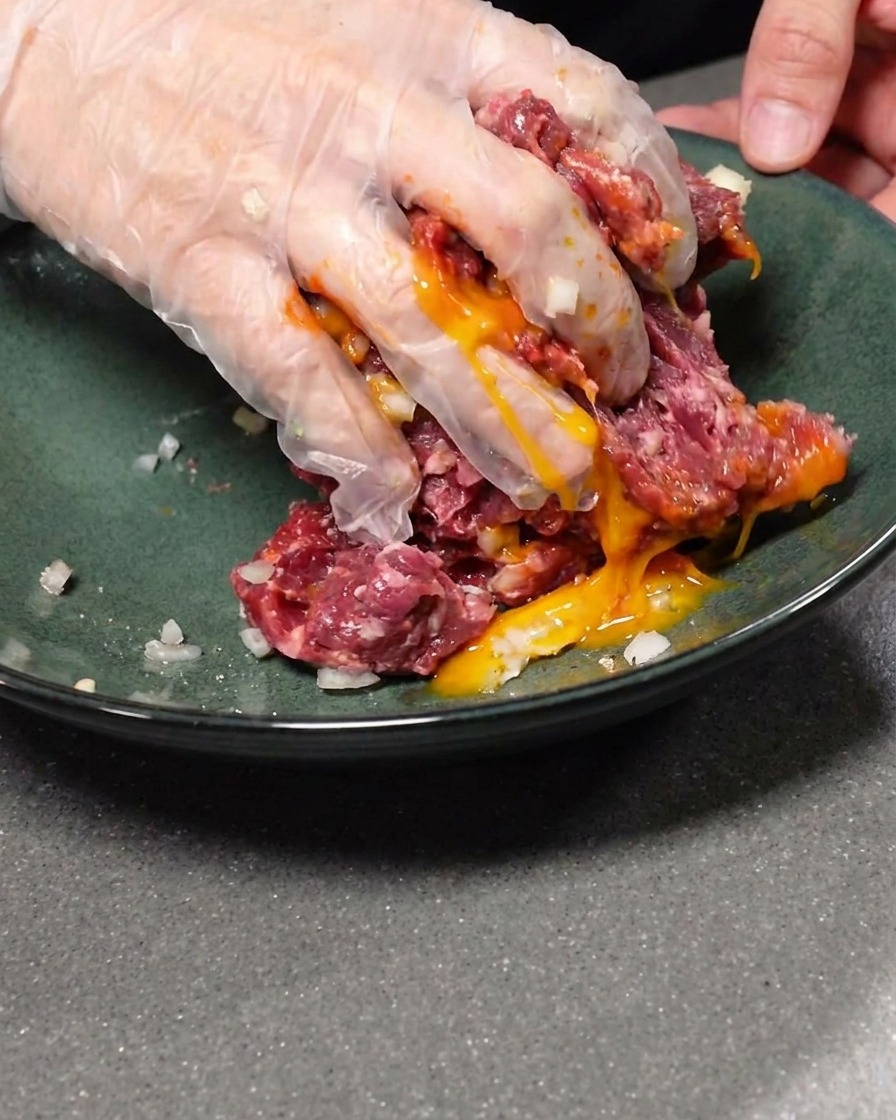 Un tuorlo duovo crudo aggiunto al composto di carne macinata condita.