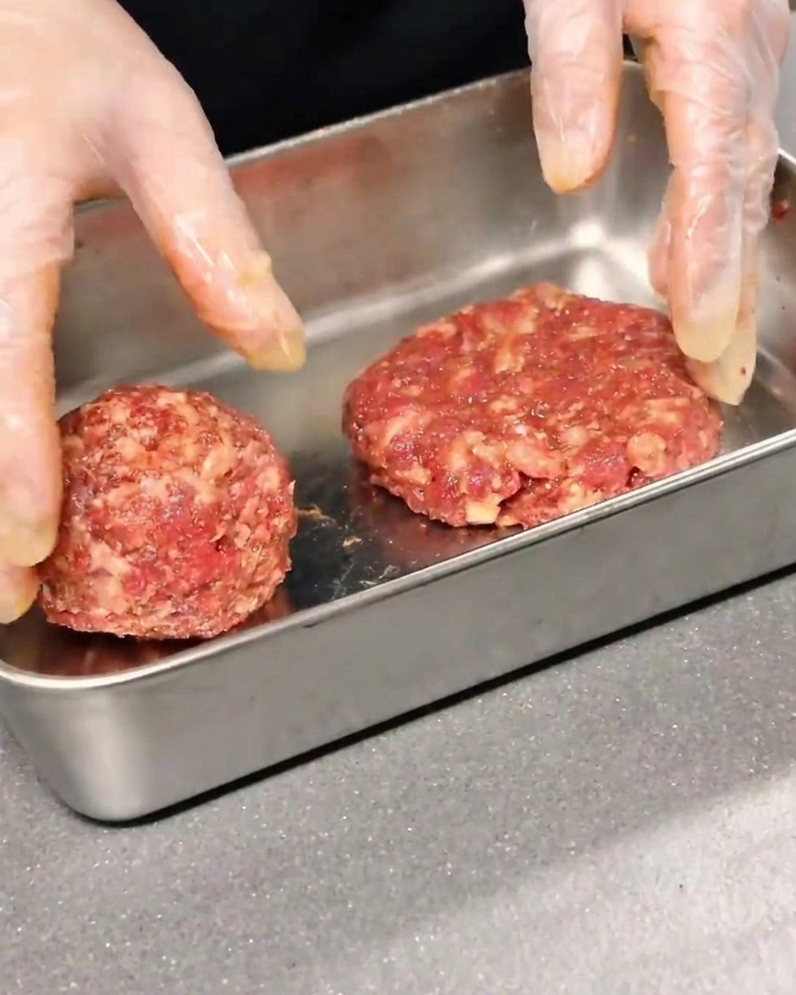 Due hamburger di manzo conditi, modellati e appiattiti in un contenitore di metallo.