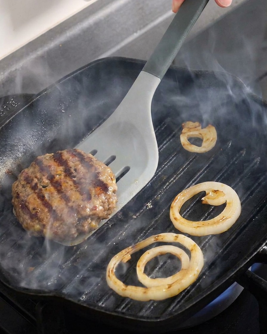 Dettaglio di un hamburger di manzo e anelli di cipolla girati su una bistecchiera calda.