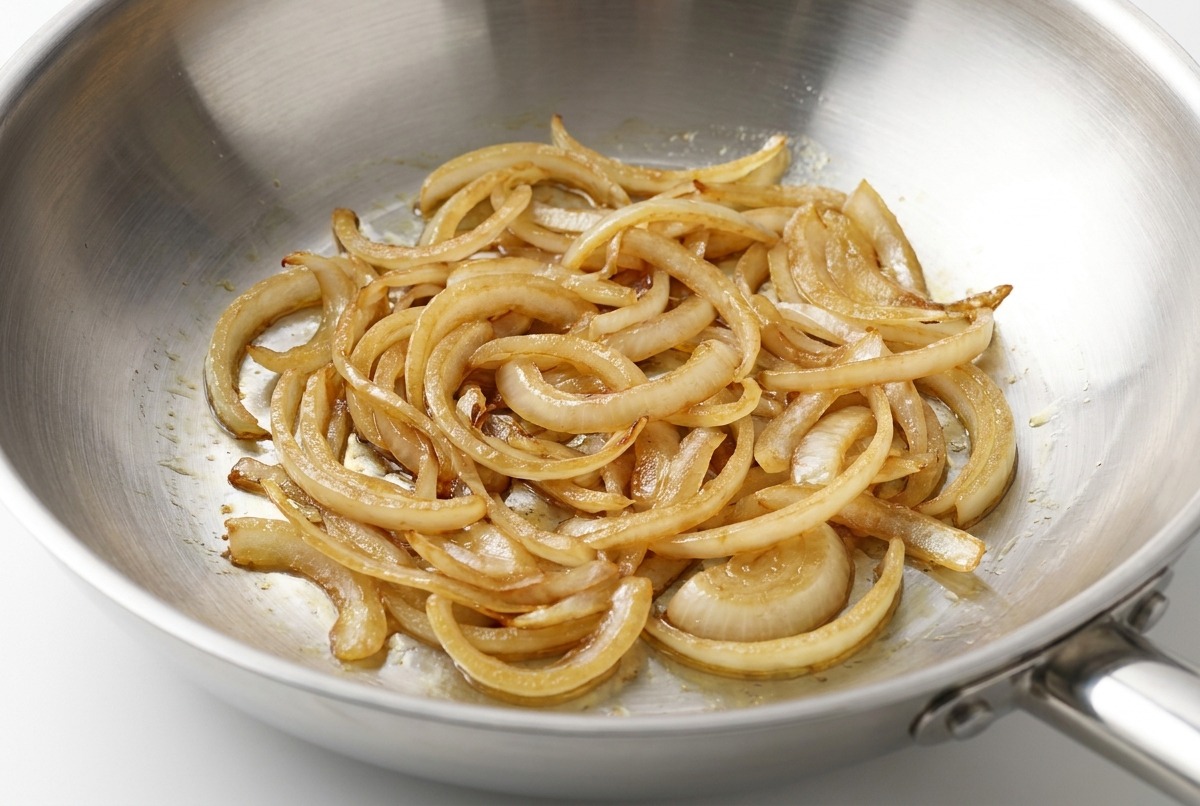 Pepe nero appena macinato aggiunto sulle cipolle saltate su una superficie di cottura.