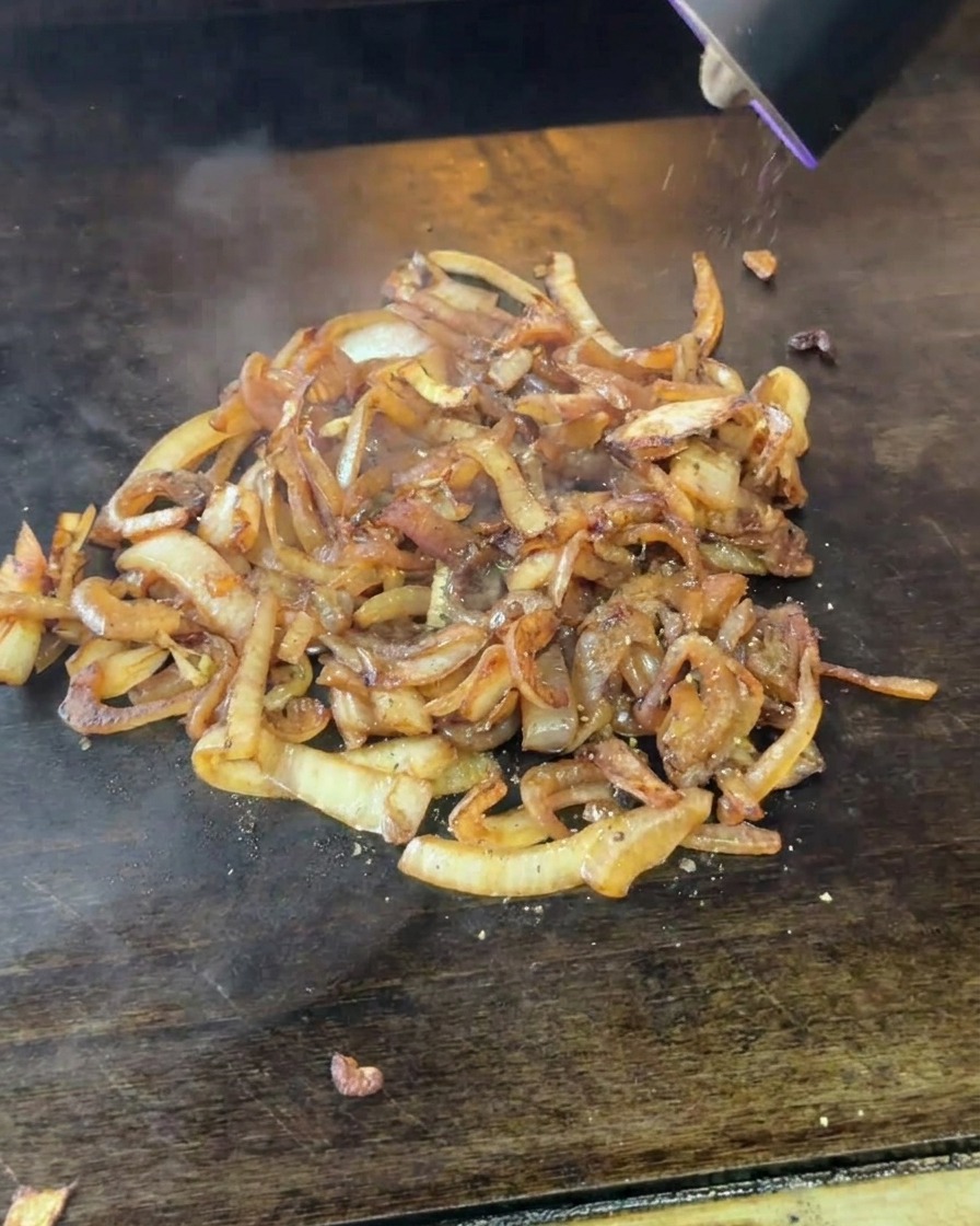 Un macinapepe elettrico che dispensa pepe nero appena macinato su un mucchio di cipolle morbide e brunite.