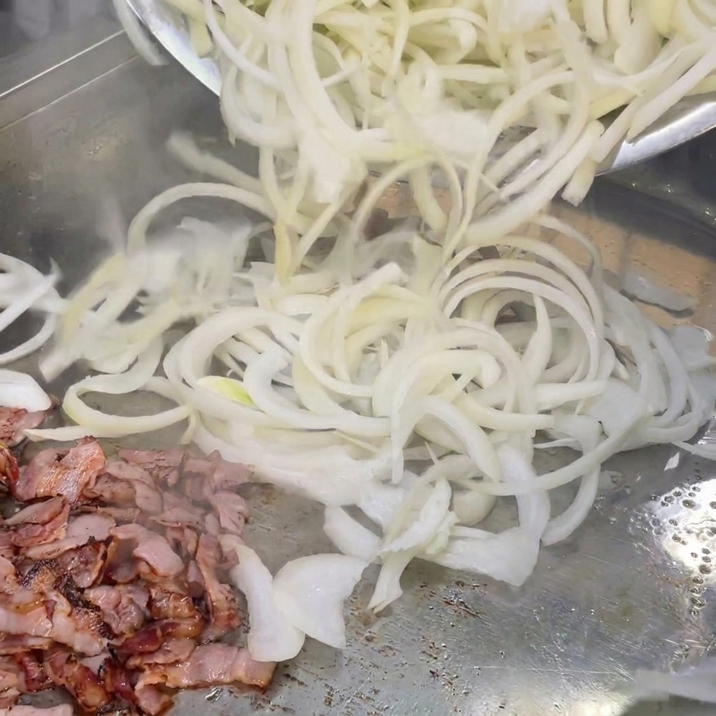 Cipolle bianche appena affettate mescolate con pezzetti di pancetta cotta su una piastra calda.
