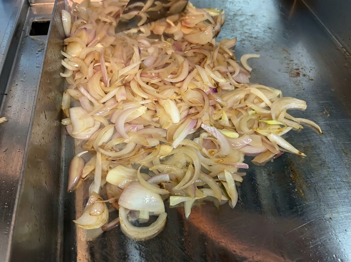 Cipolle affettate mescolate continuamente con una spatola su una piastra calda per farle ammorbidire e caramellare.