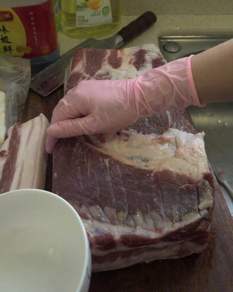 Un grande pezzo di pancetta cruda viene strofinato con liquore bianco su un tagliere di legno.