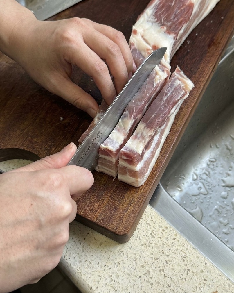 La pancetta cruda viene tagliata in strisce lunghe e spesse con un coltello da cucina affilato.