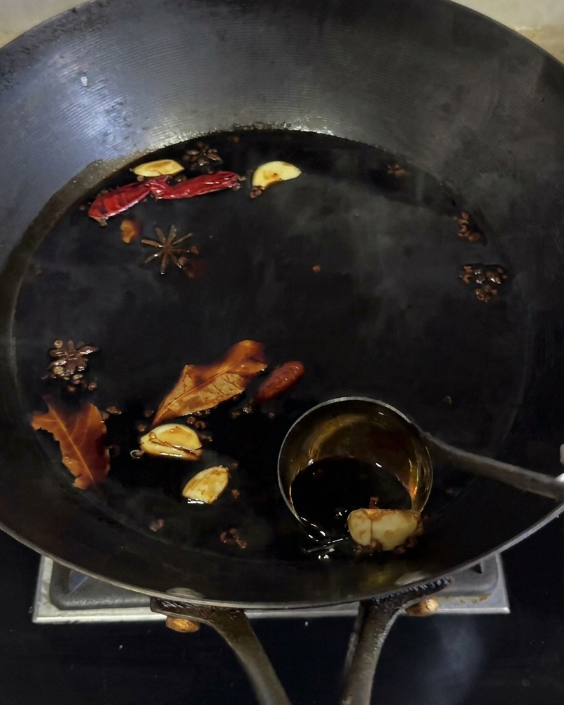 La marinata di salsa di soia scura sobbolle in un wok con vari aromi come anice stellato e aglio.