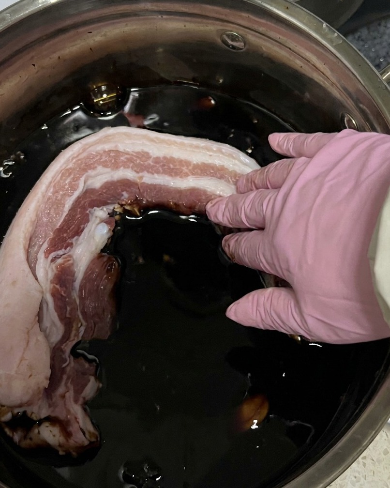 Strisce di pancetta cruda vengono immerse in una pentola con la marinata di salsa di soia scura.