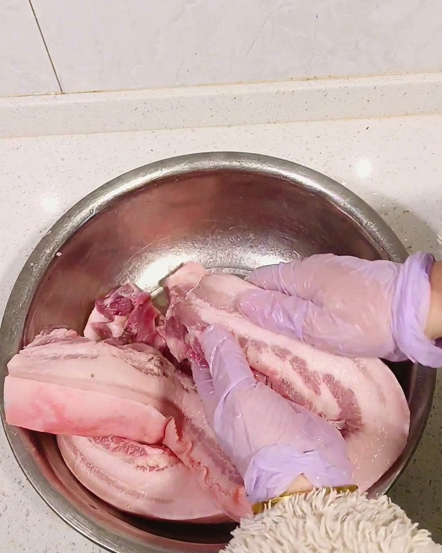 Mani con guanti viola massaggiano il distillato nella carne cruda.