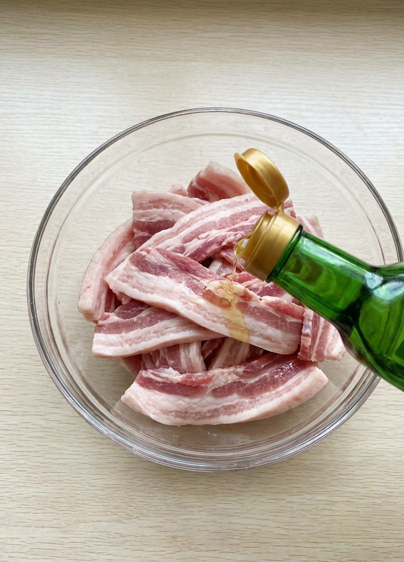 Salsa di soia versata da una bottiglia di vetro sopra le strisce di pancetta cruda in una ciotola.