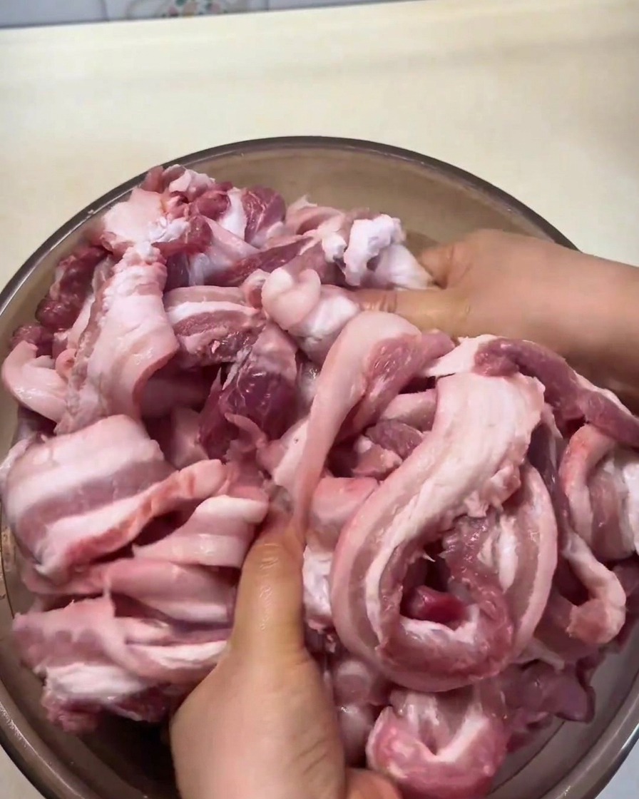 Strisce di pancetta massaggiate a mano con spezie e condimenti allinterno di una ciotola.