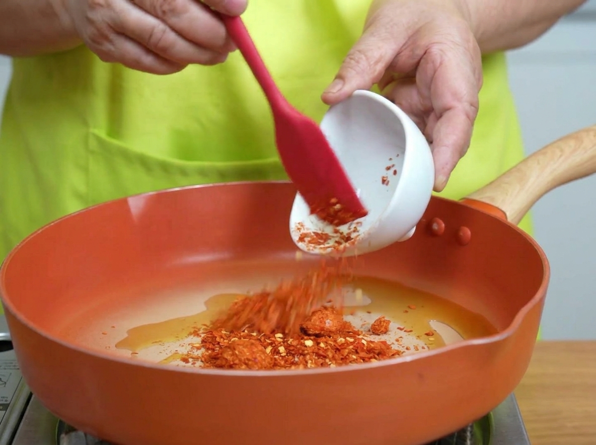 Fiocchi di peperoncino mescolati nellolio caldo sfrigolante in padella.