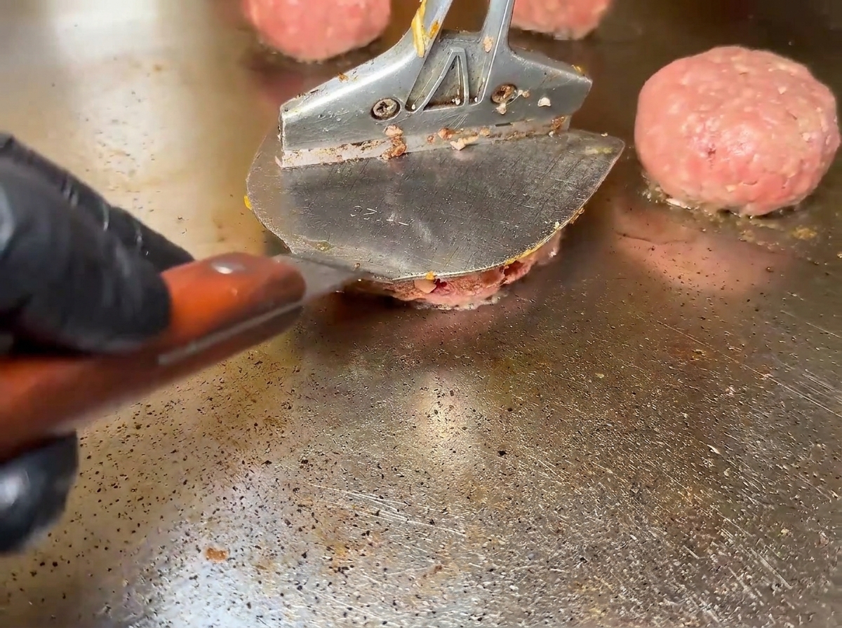Hamburger di manzo crudi che sfrigolano su una superficie calda.