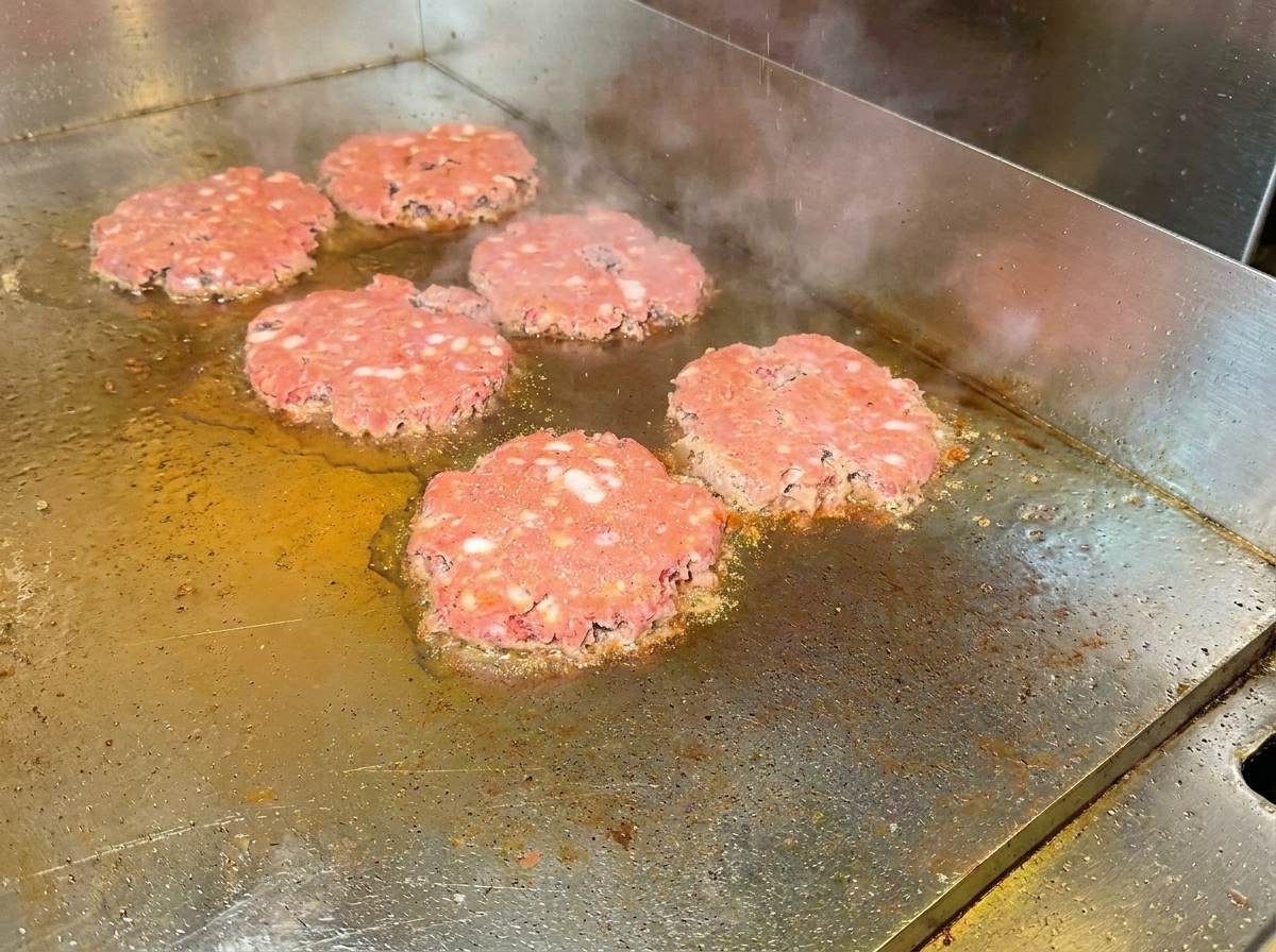 Hamburger girati sulla piastra, che mostrano una superficie ben rosolata e le spezie.